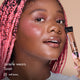 Janelle wearing HD PRO.Conceal Toast and holding the tube beside her cheek.