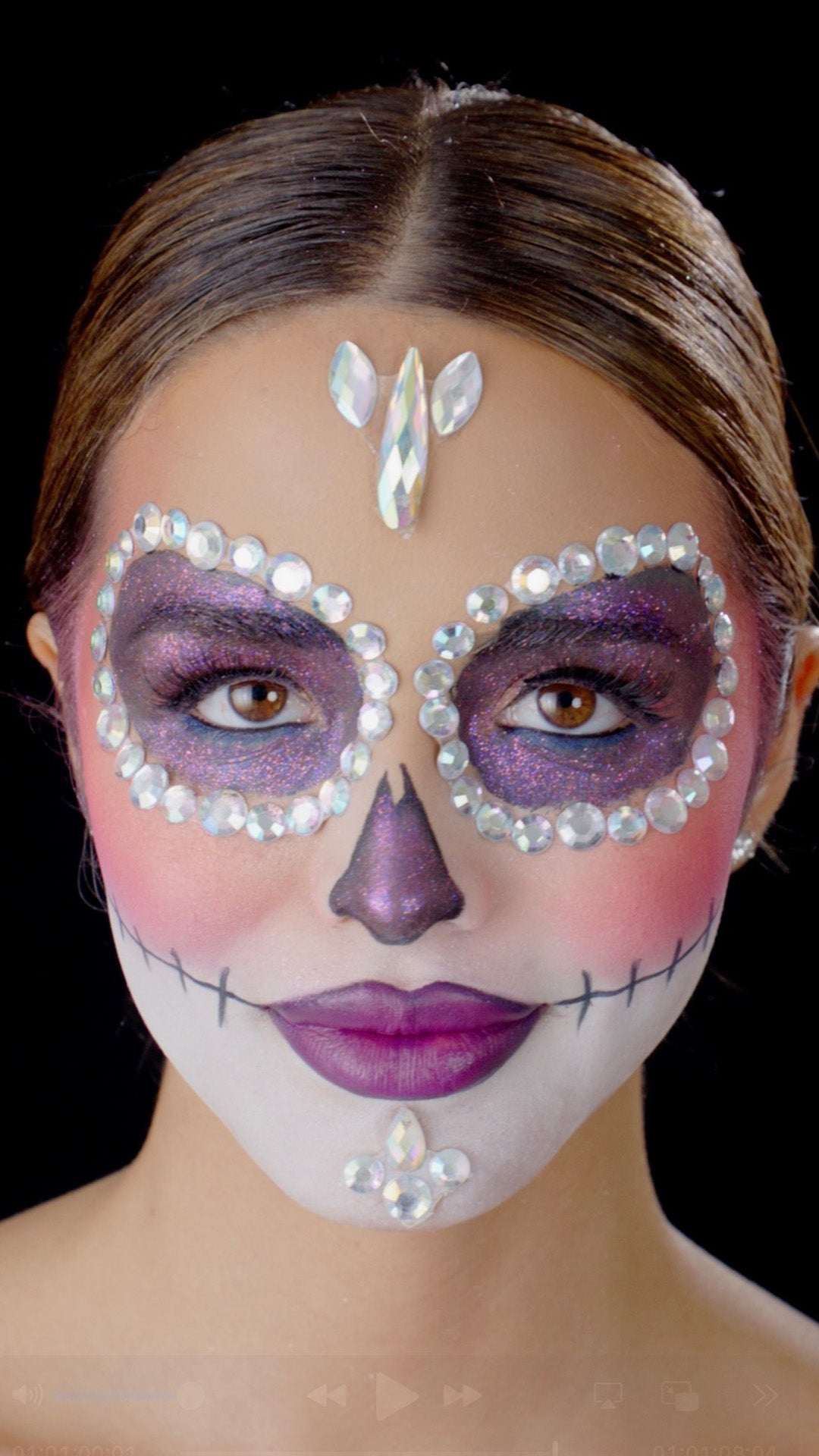 L.A. Girl Moonlit Bloom Face Gems look thumbnail: model with purple jeweled sugar-skull eye masks and a purple lip